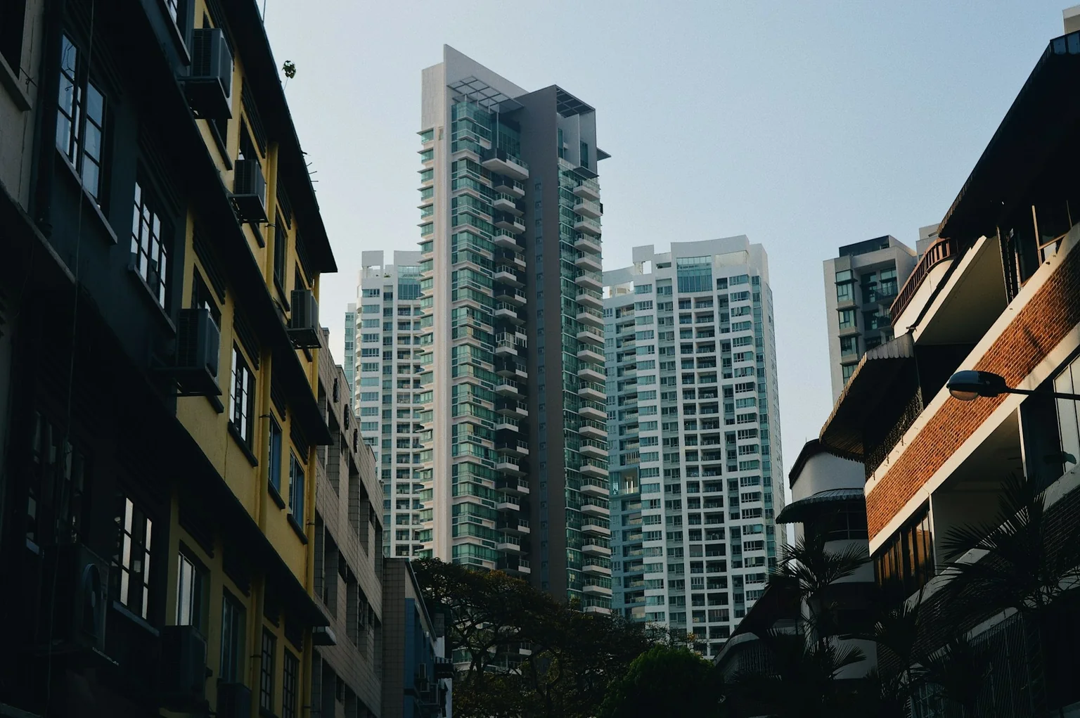 Residential towers rising behind shaded low-rise neighbourhood buildings in Tiong Bahru.